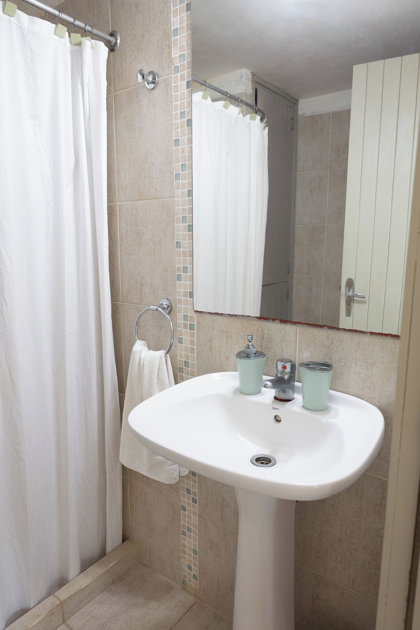 Een badkamer met een witte wastafel, een handdoekhouder, een douchegordijn en een spiegel.