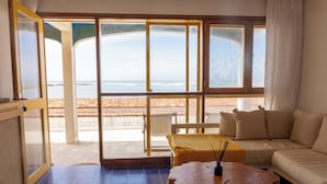 A room with a large sliding glass door leading to a terrace with a view of the sea. There is a sofa and a wooden coffee table with a candle in the room. - Apartamentos Alborada (La Paloma)