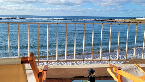 A balcony with a view of the sea, a table with a mug and a plate of food, and a chair. - Apartamentos Alborada (La Paloma)