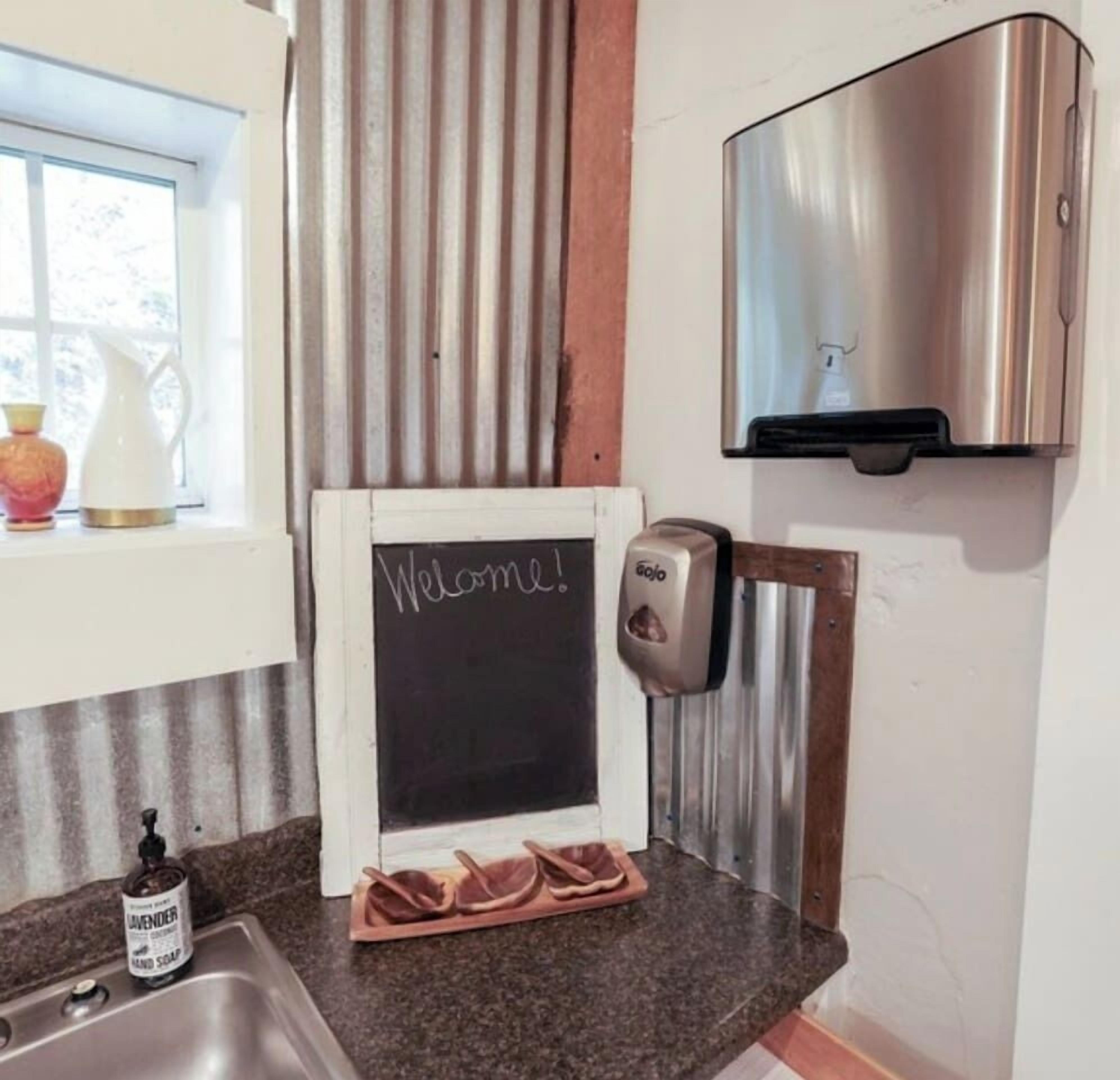 A kitchen with a chalkboard sign saying "Welcome!", a soap dispenser, and a bottle of hand soap.