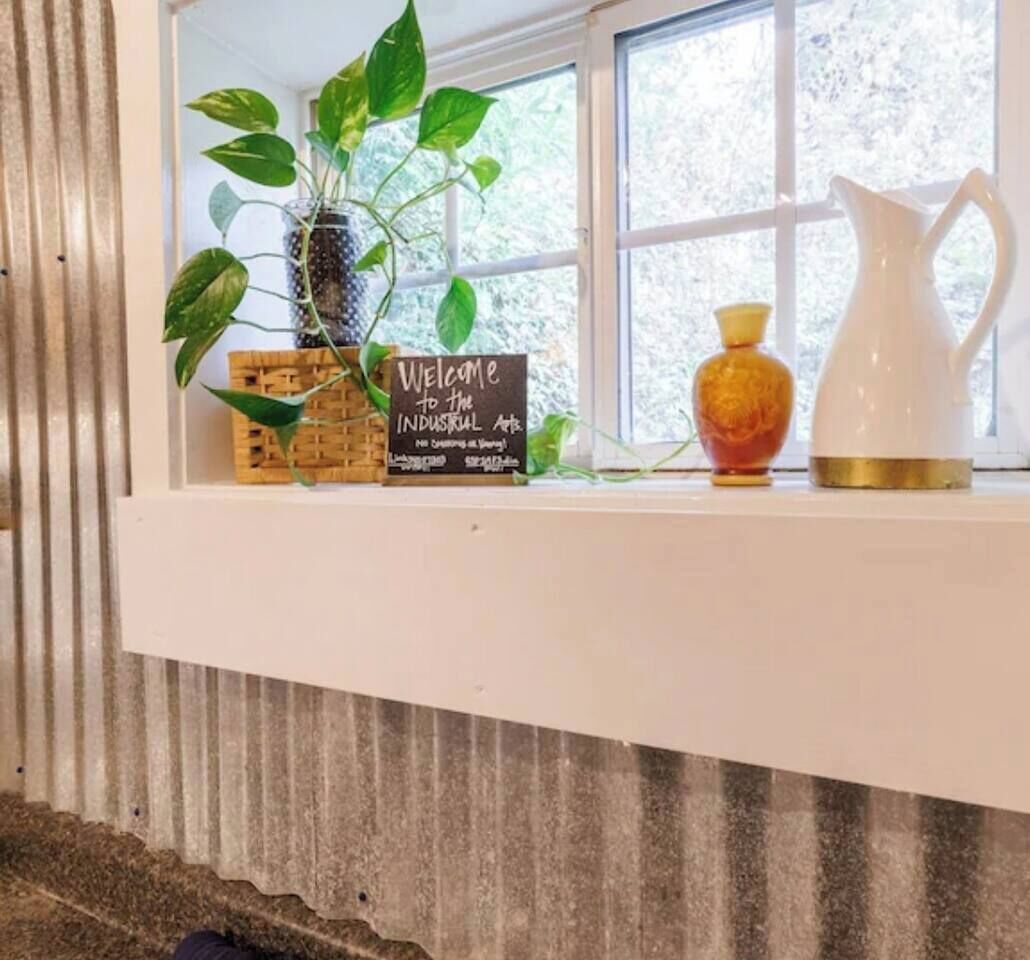 A window ledge with a welcome sign, a potted plant, a vase, and a pitcher.