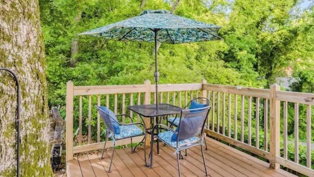 A wooden deck with a table and chairs, surrounded by a wooden railing and lush green trees.