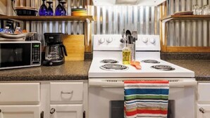 A kitchen with a white stove, a microwave, and various kitchen items on shelves.