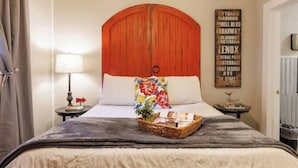 A bedroom with a large bed, a wooden headboard, a bedside table with a lamp, and a wall with a list of street names.