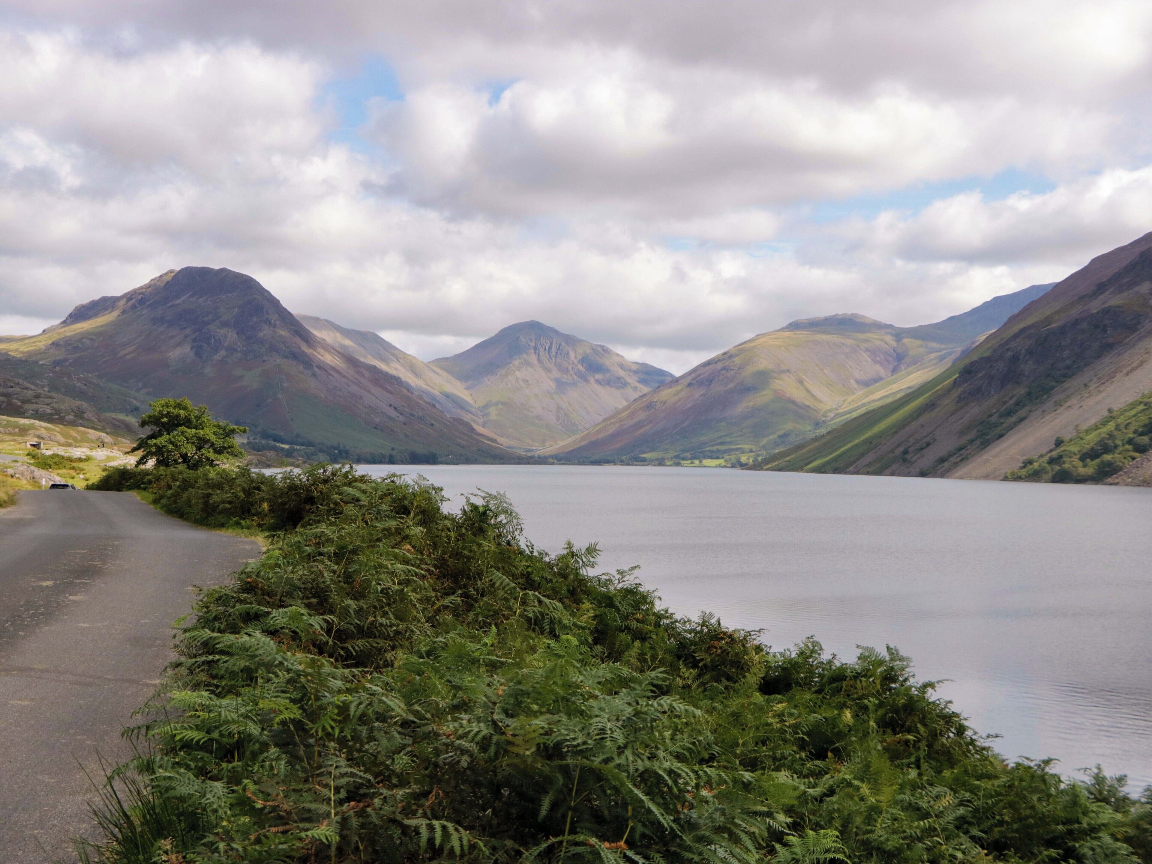 A scenic mountain road leading to a lake with lush greenery and mountains in the background.