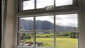 Ventana con vista a un paisaje montañoso y un campo verde con coches estacionados.