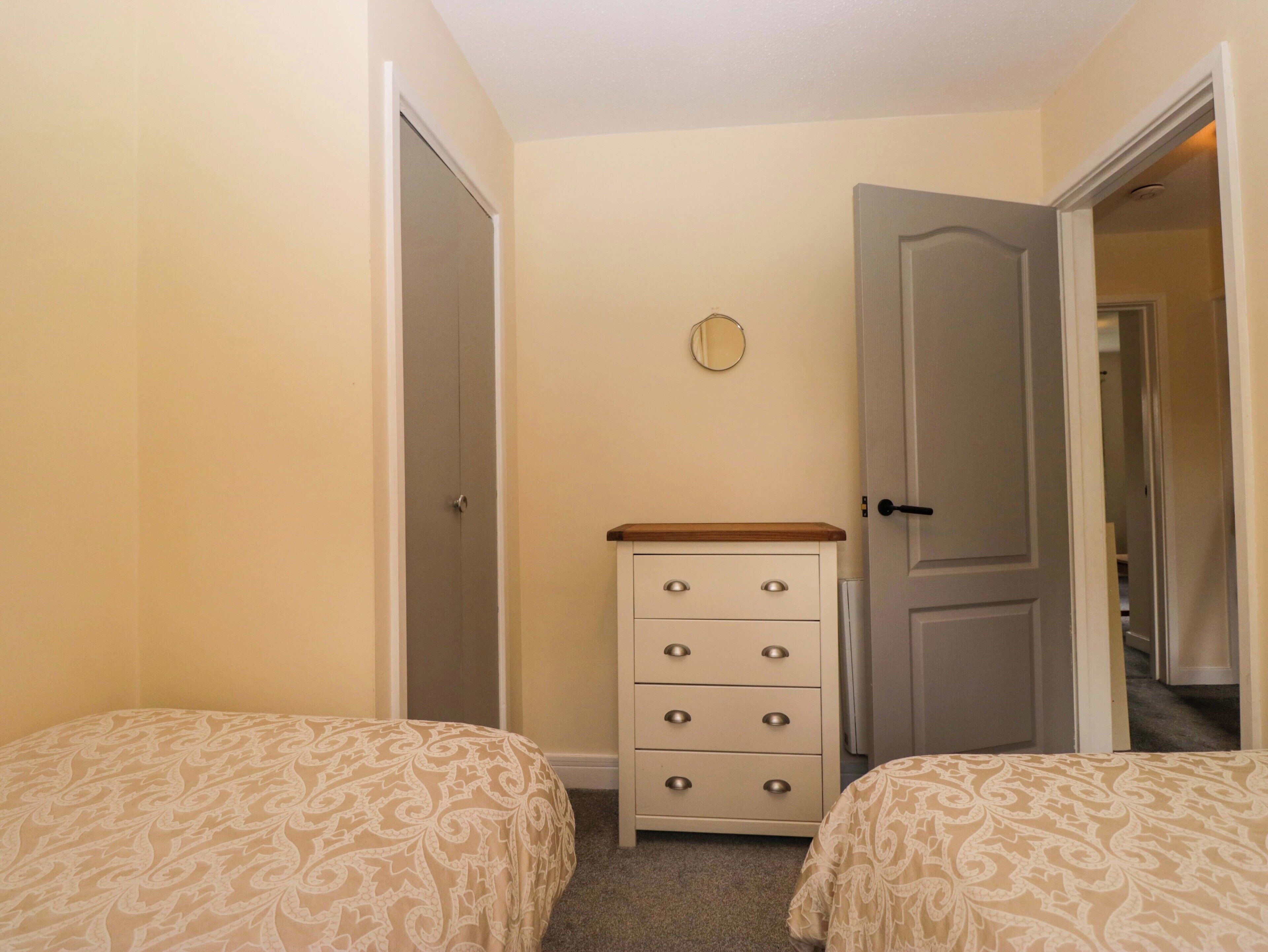 A bedroom with two beds, a dresser, and a door leading to another room.