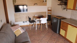 A compact living space with a sofa, dining table, chairs, and a kitchenette.