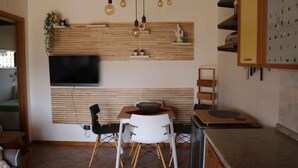 A modern kitchen with a wooden wall-mounted shelf, a flat-screen TV, and a dining area with a table and chairs.
