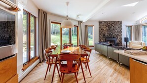 A modern kitchen with a dining area, large windows, and a stone fireplace. - Dreamwood: A Modern Catskills Retreat (Jeffersonville)