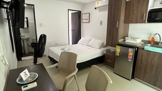 A compact hotel room with a bed, a desk, a chair, a kitchenette, and a bathroom. - Smart Lychee Studio Apartment #1 (Montería)