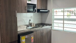 Cozinha compacta com armários de madeira, geladeira de aço inoxidável, micro-ondas e janela com vista para prédios.