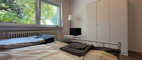 A bedroom with a bed, a TV, a wardrobe, and a window with a view of trees.