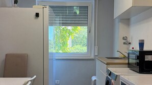 A compact kitchen with a washing machine, a refrigerator, and a dining area with a table and chairs. - Three Bedroom Comfort Apartment Maintal (Maintal)