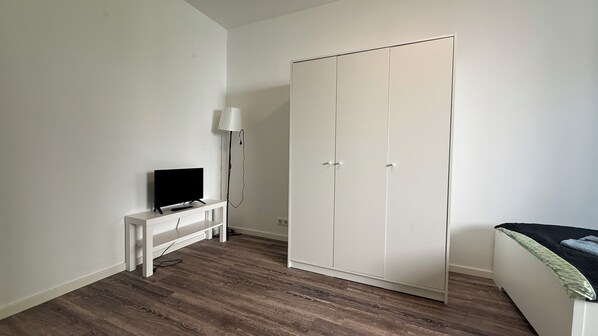 Un dormitorio con cama, armario, televisor sobre un mueble bajo y lámpara de pie.