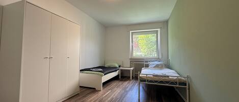 Un apartamento pequeño de una sola habitación, con un armario grande, una ventana con vistas a zonas verdes y un radiador.