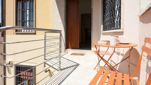 A small outdoor seating area with a table and chairs, a metal railing, and a door leading to an interior space. - Vatican Secret Apartment (Rome)
