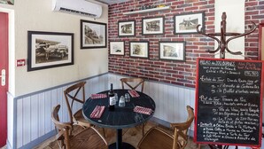 A corner restaurant with a brick wall, framed pictures, a round table with chairs, and a chalkboard menu. - RELAIS LES 200 BORNES  (Pouilly-sur-Loire)