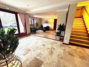 A hotel lobby with a tiled floor, a staircase, and a seating area with chairs and a table. - RELAIS LES 200 BORNES (Pouilly-sur-Loire)
