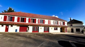 A two-story building with a red-tiled roof and white walls, featuring multiple red shutters and a garage door. - RELAIS LES 200 BORNES  (Pouilly-sur-Loire)