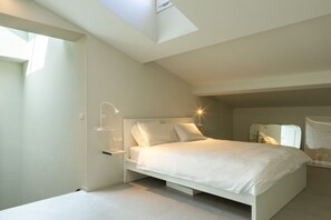 Ein modernes Schlafzimmer mit Dachfenster, einem Bett mit weißer Bettwäsche und einem Nachttisch mit Lampe.