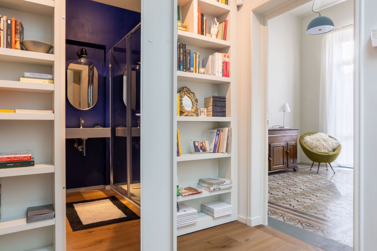 A room with a bookshelf, a mirror, a chair, and a patterned rug.