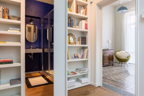 Ein Zimmer mit Bücherregal, Spiegel, Stuhl und einem gemusterten Teppich.