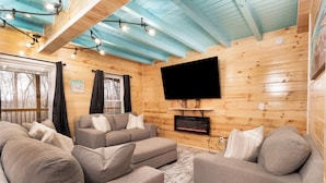 A cozy living room with a large flat-screen TV mounted on the wall, a fireplace, and a wooden ceiling. - Margaritahills is the perfect getaway for  two couples, where rustic elegance meets modern comfort. (Creola)