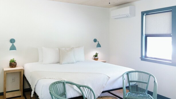 A bedroom with a bed, two chairs, a wooden stool, a ceiling fan, and a window.