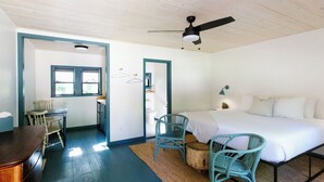 A bedroom with a bed, two chairs, a desk, and a ceiling fan.