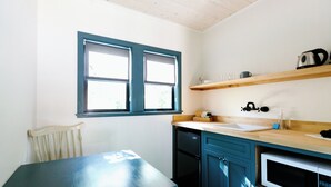 A kitchen with a wooden table, blue cabinets, a microwave, and a window with blinds.