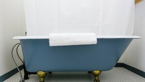 Une baignoire bleue sur pieds, avec une serviette blanche, posée sur un sol carrelé.