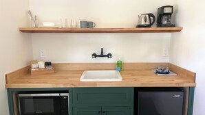 Eine kompakte Küche mit einer Mikrowelle, einem Kühlschrank, einer Spüle und einer Kaffeemaschine auf einem Regal.