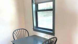 Ein Zimmer mit einem dunklen Holztisch und -stühlen, einem Fenster mit Blick auf Grünflächen und einer weißen Wand.