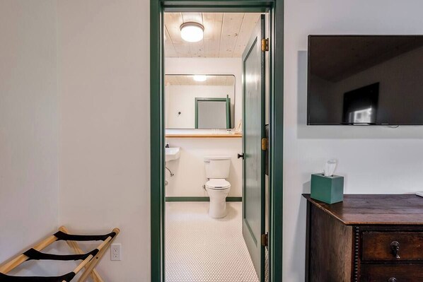 A bathroom with a toilet, sink, mirror, and a wooden cabinet with a tissue box.