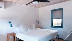 A bedroom with a bed, a nightstand, a ceiling fan, a window, and a wall-mounted air conditioner. - Amber Cottage at Piety Hill Cottages (NEVADA CITY)