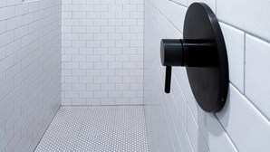A modern bathroom with white tiled walls and floor, a wooden ceiling, and a black showerhead.