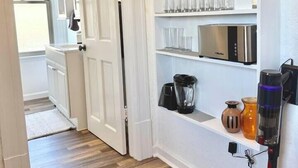 Une cuisine avec des meubles blancs, un four à micro-ondes, un mixeur et une machine à café posés sur le plan de travail.