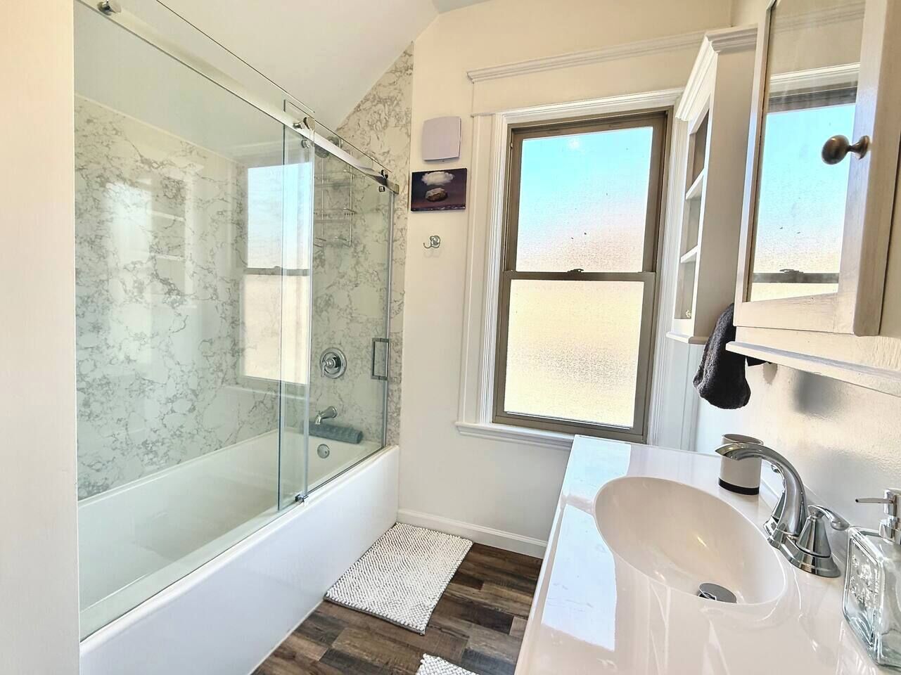 A modern bathroom with a glass-enclosed shower, a white sink, and a window providing natural light.
