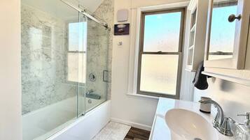 A modern bathroom with a glass-enclosed shower, a white sink, and a window providing natural light.