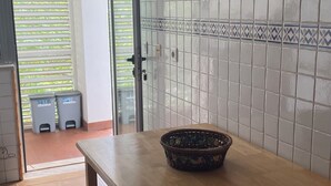 A kitchen with white tiled walls, a wooden table, and two trash bins.