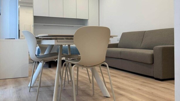 Una sala de estar moderna con zona de comedor, que presenta un sofá de color claro, una mesa redonda y un diseño minimalista.