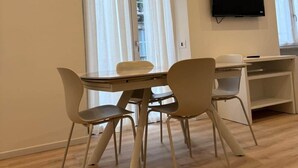 Un comedor moderno con una mesa y sillas, un televisor de pantalla plana en la pared y ventanas grandes con cortinas.