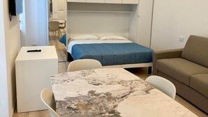 Una habitación compacta con cama, sofá, una mesita y televisor instalado en la pared.