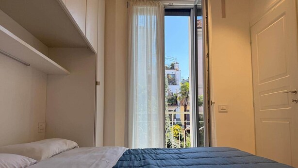 Une chambre à coucher avec un lit, une fenêtre avec des rideaux et une vue sur les bâtiments à l’extérieur.