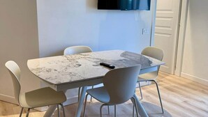 Un espace repas moderne avec une table en marbre, des chaises blanches et un téléviseur à écran plat fixé au mur.