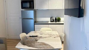 Une cuisine compacte équipée d’un four à micro-ondes, d’un réfrigérateur et d’un petit plan de travail sur lequel se trouvent une bouilloire et une plante.