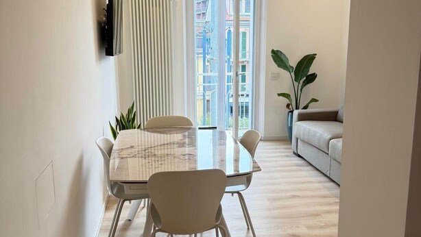 A modern living room with a sofa, a dining table with chairs, a potted plant, and a view through a glass door. - Apartment Basilica of Sant'Ambrogio (Milan)