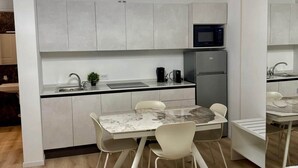 A compact kitchen with a microwave, coffee maker, and a small sink. There is a dining table with chairs and a bed with a mattress.