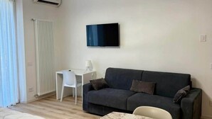 A modern living room with a dark sofa, a white table, and a TV mounted on the wall.